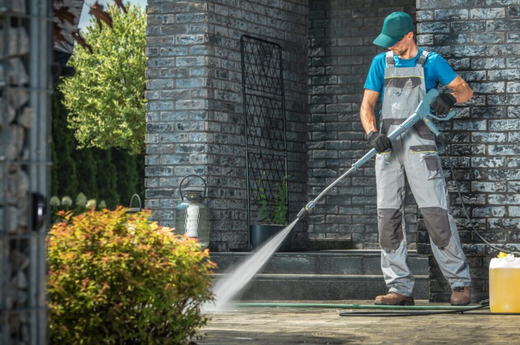 Driveway Pressure Washing. Caucasian Worker Cleaning Area in Front of the House.

\How to Save Money on Exterior Cleaning